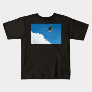 Snowboarder jumping against blue sky Kids T-Shirt